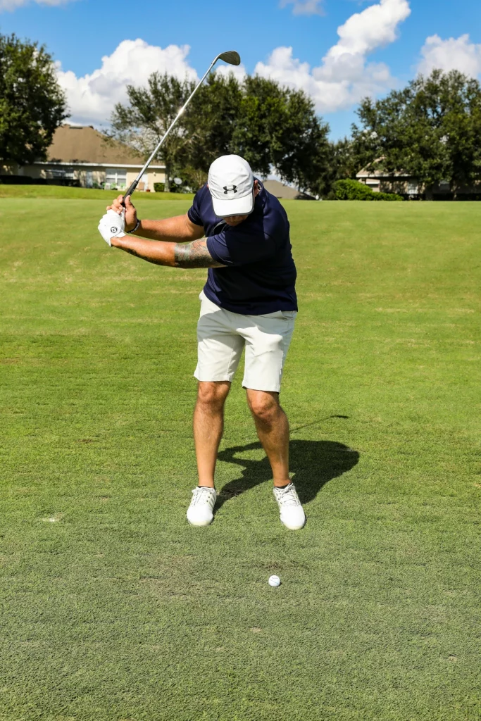 Golfista en backswing corto con wedge durante un golpe de approach