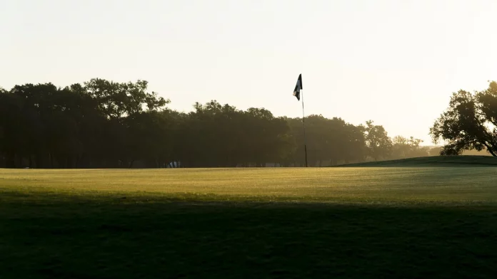 Green de golf iluminado por la luz del atardecer, con bandera visible al fondo