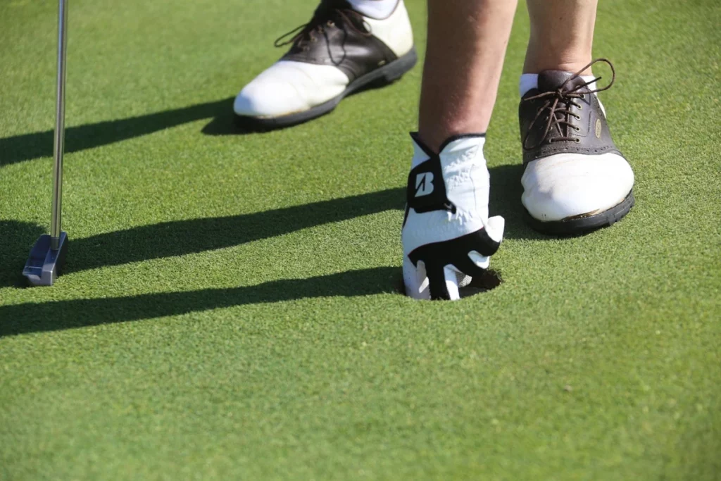 Jugador de golf recogiendo la bola del hoyo tras completar un putt en el green