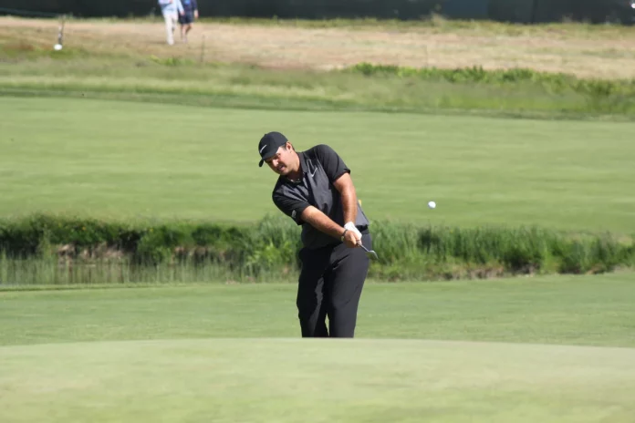 "Patrick Reed usando un hierro para un approach durante una práctica en el campo de golf."