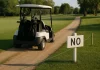 Carrito de golf circulando por el camino junto al fairway con señal de prohibición