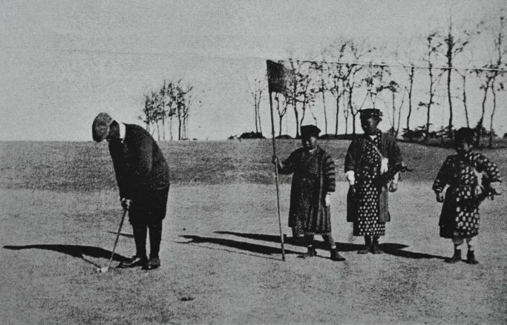 Caddies japoneses en el Tokyo Golf Club, Komazawa Course, vestidos con ropa tradicional, en una fotografía en blanco y negro.