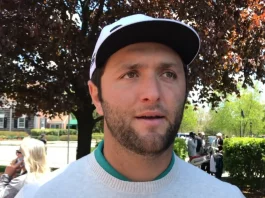 Jon Rahm durante una rueda de prensa oficial, vistiendo polo gris y gorra blanca, primer plano con fondo neutro